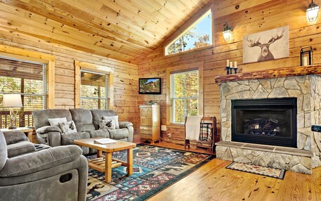 A cozy log cabin interior with a fireplace, comfortable seating, and large windows.
