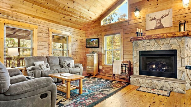 A cozy log cabin interior with a fireplace, comfortable seating, and large windows.