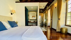 A spacious bedroom with a large bed, a bathroom with a sink and mirror, and a view of the outside through a glass door.
