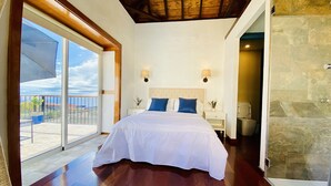 A bedroom with a large bed, a sliding glass door to a balcony, a stone wall, and a wooden ceiling.