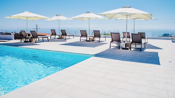 A poolside area with lounge chairs and umbrellas, a clear sky, and a view of the ocean.