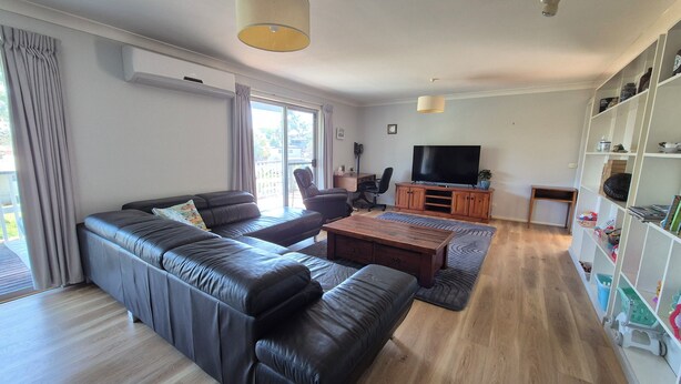 A modern living room with a leather sofa, a wooden coffee table, a TV, and a bookshelf. - Catalina Coastal Getaway / Family friendly home (Catalina)