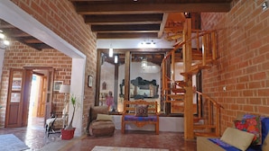 Un vaste espace de vie agrémenté d’un mur en briques, d’un escalier en bois et d’un coin salon confortable comprenant un canapé et un banc.