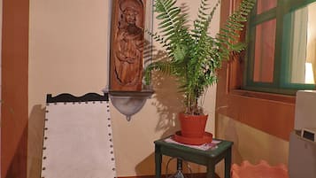 A room with a wooden bench, a potted plant, a wall-mounted sculpture, and a window with a green frame.