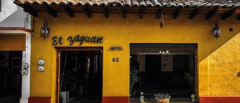 Un edificio amarillo con un letrero que dice "El Zaguán HOTEL 65" y un techo de tejas.