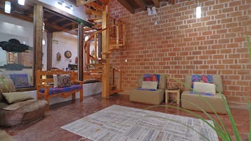 A cozy living room with a brick wall, wooden furniture, and a spiral staircase.
