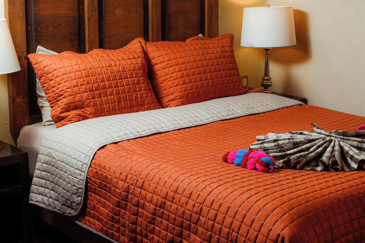 A bed with a quilted orange blanket, pillows, and a white quilted bedspread.
