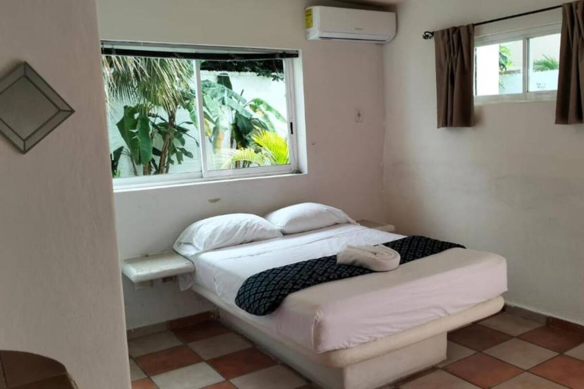 Una cama individual con ropa blanca, una ventana con cortinas, un equipo de aire acondicionado y vistas a zonas verdes.