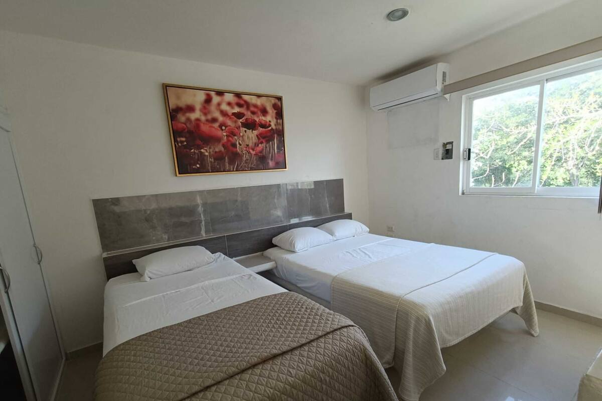 Una habitación de hotel con dos camas, un ventanal grande y un equipo de aire acondicionado.