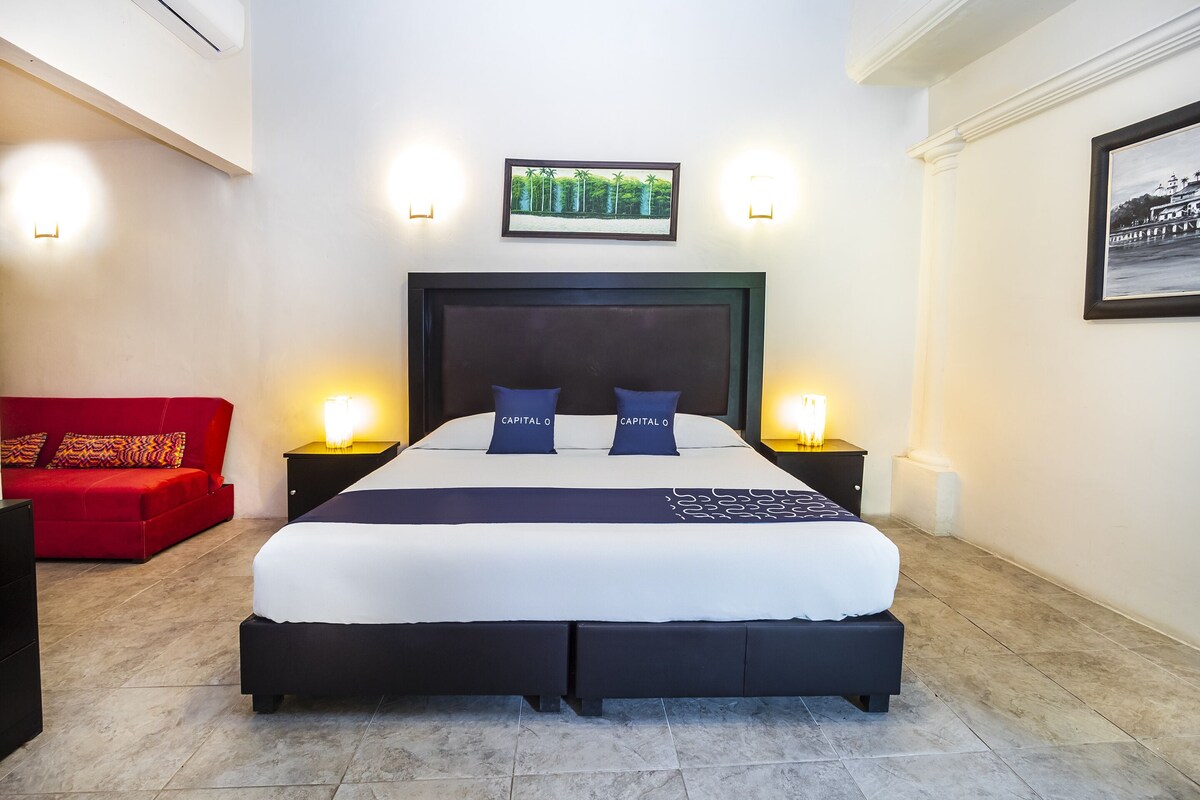 A large bed with a dark headboard, two pillows labeled "Capital O", and a framed picture above.