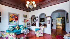 Un amplio salón con un sofá azul, sillas de colores, una araña y vistas hacia un comedor.