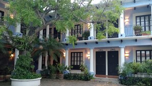 Edificio de dos plantas con un patio interior, con macetas, una palmera y una entrada bien iluminada con puertas numeradas.