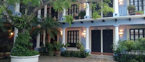 Edificio de dos plantas con un patio interior, con macetas, una palmera y una entrada bien iluminada con puertas numeradas.