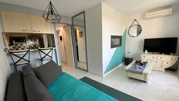 A modern living room with a sofa, a coffee table, and a TV. There is a kitchen area with a microwave and a dining table. - T2 air-conditioned apartment with swimming pool close to grande plage richelieu (Agde)