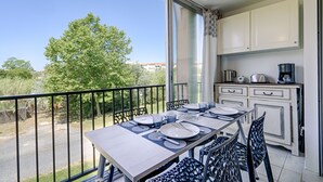 A balcony with a dining table set for four, white cabinets, and a coffee maker. - T2 air-conditioned apartment with swimming pool close to grande plage richelieu (Agde)
