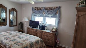 Un dormitorio con cama, cómoda, televisor y ventana con cortinas.