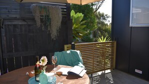 A round wooden table with a book, a glass of wine, and a vase with a flower. - Beach, Cafes, Golf, Sun & Privacy at Paraparaumu Beachside Studio w sea view (Paraparaumu)