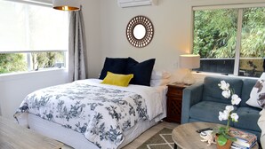 A bedroom with a bed, bedside table, lamp, and a view of greenery outside. - Beach, Cafes, Golf, Sun & Privacy at Paraparaumu Beachside Studio w sea view (Paraparaumu)