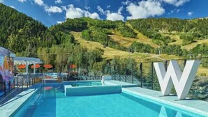 Una piscina con montañas al fondo, una gran letra 'W' blanca, y una zona cubierta con sombrillas.