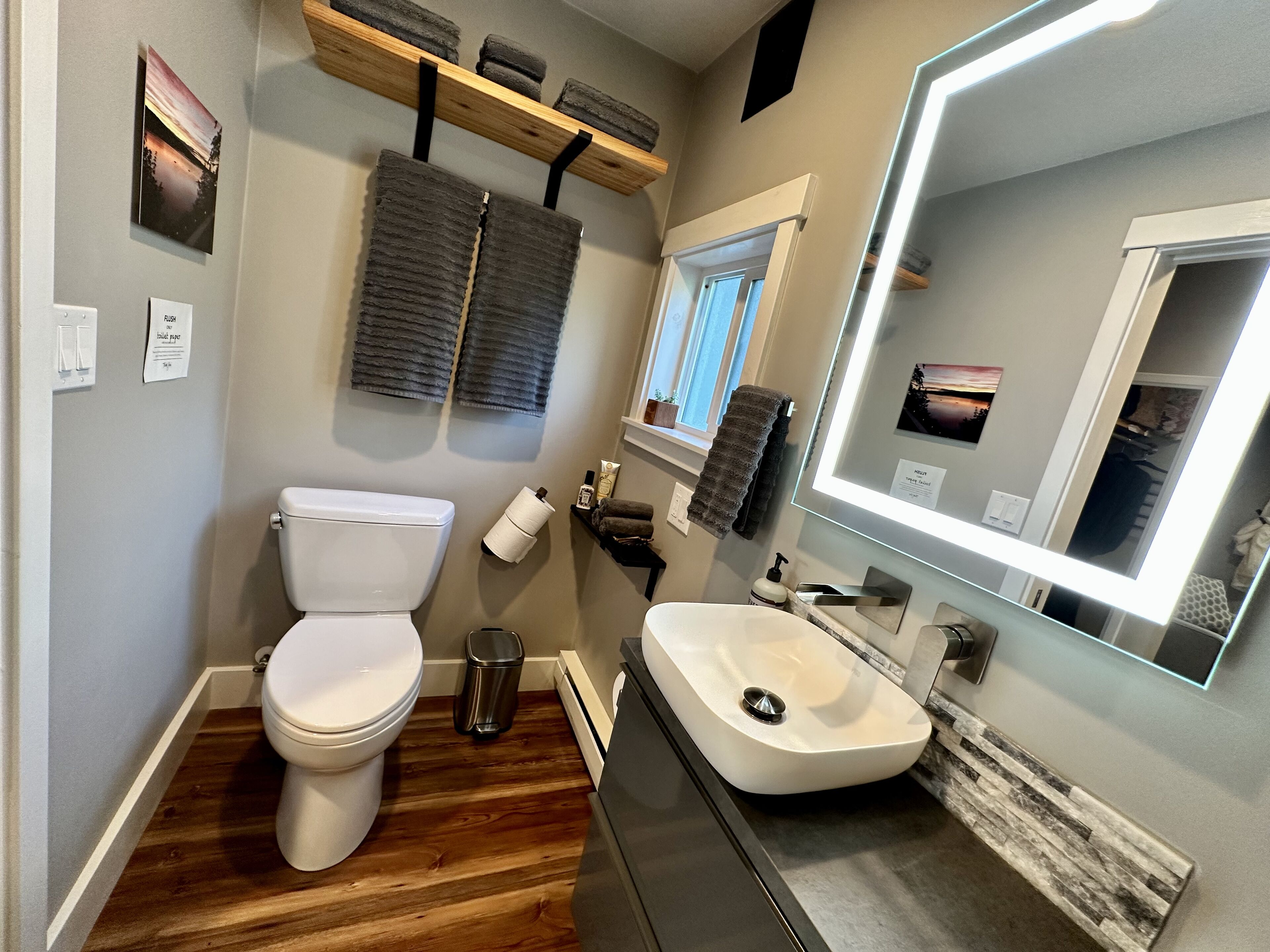 A bathroom with a toilet, sink, and mirror. There are towels hanging on a rack and a trash can.
