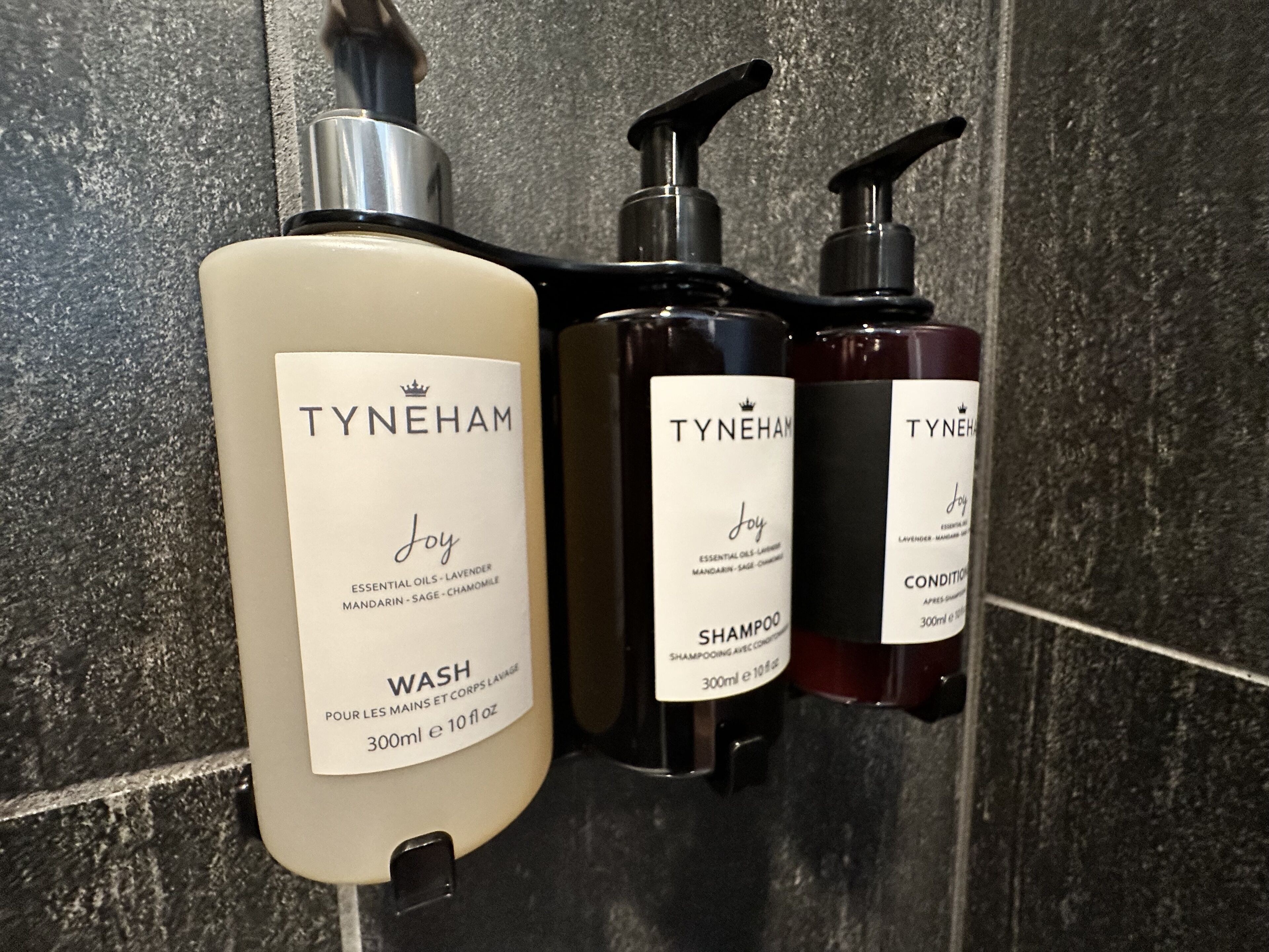 Three bottles of TYNEHAM Joy products: a 300ml wash, a 300ml shampoo, and a 300ml conditioner, all with pump dispensers.