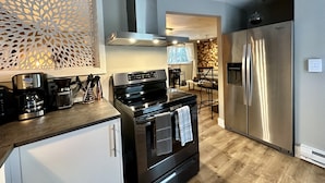 A modern kitchen with stainless steel appliances, a coffee maker, and a decorative wall panel.
