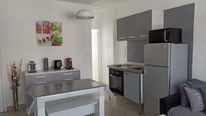 A modern kitchen with grey cabinets, a stainless steel refrigerator, a microwave, and a gas stove. There is a dining table with a white tablecloth and a vase with dried plants. - Les Chevalets II/ University/Louvre/Bollaert (Lens)