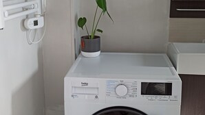 A compact, white front-loading washing machine with a digital control panel, a small trash bin, and a potted plant on top. - Les Chevalets II/ University/Louvre/Bollaert (Lens)