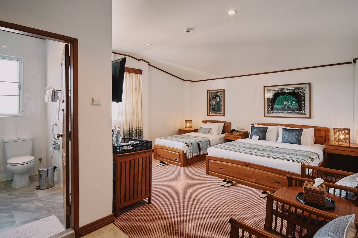 A hotel room with a large bed, a smaller bed, a desk, a chair, a bathroom with a toilet and shower, and two framed pictures on the wall.