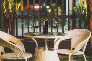 A round table with a bottle and two glasses of red wine, surrounded by wicker chairs. - Winner Inn (Yangon)