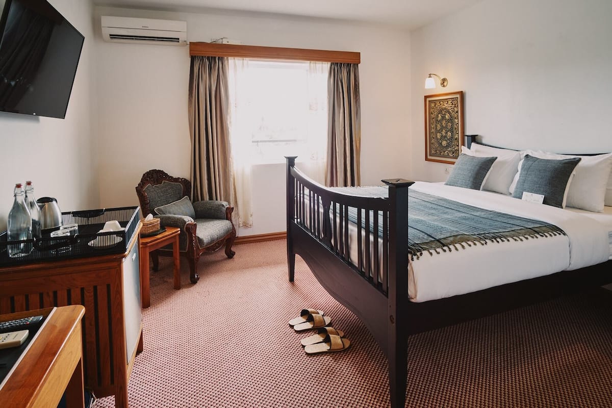 A bedroom with a bed, a chair, a desk with a computer, and a TV.