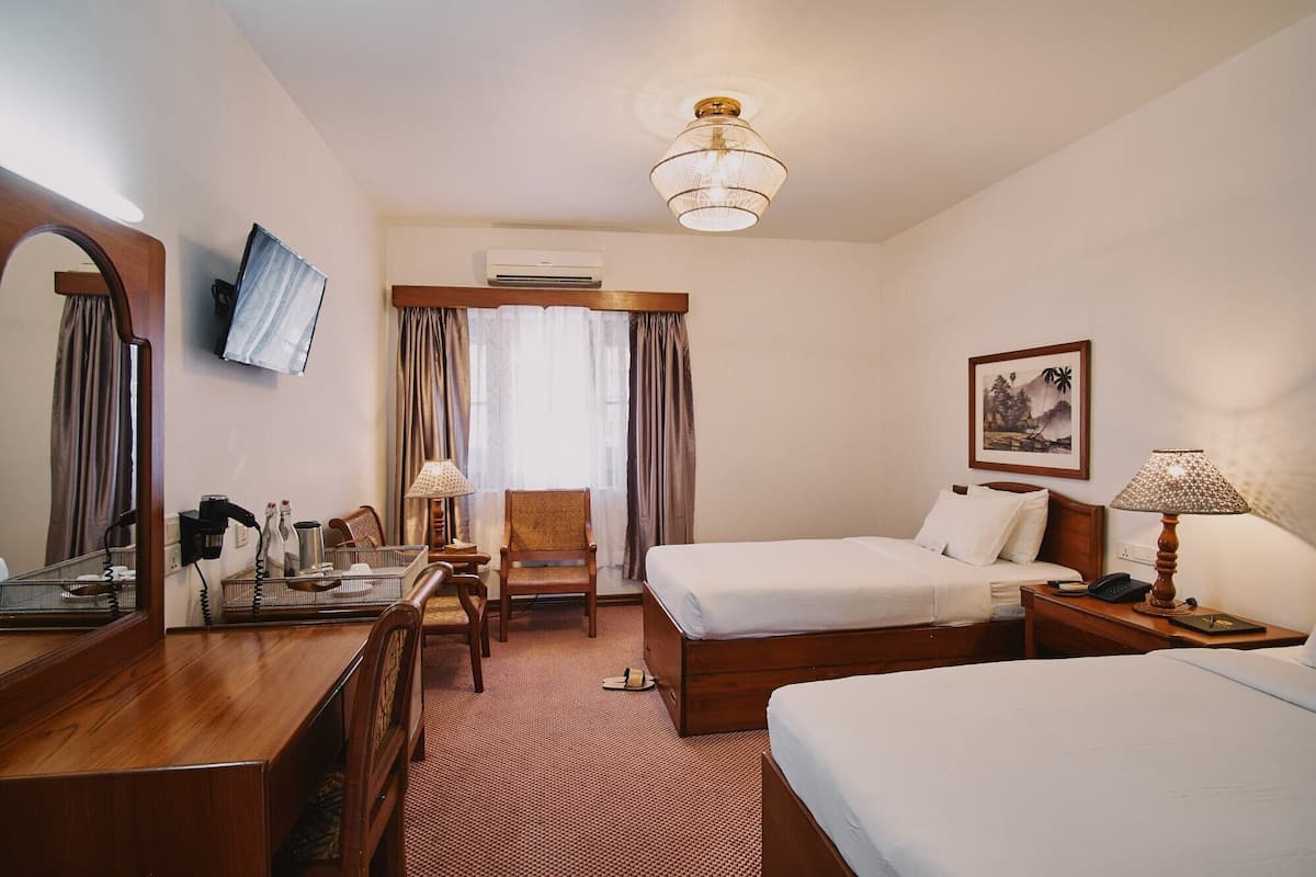 A hotel room with two beds, a desk with a chair, a mirror, a TV, an air conditioning unit, and a framed picture on the wall.