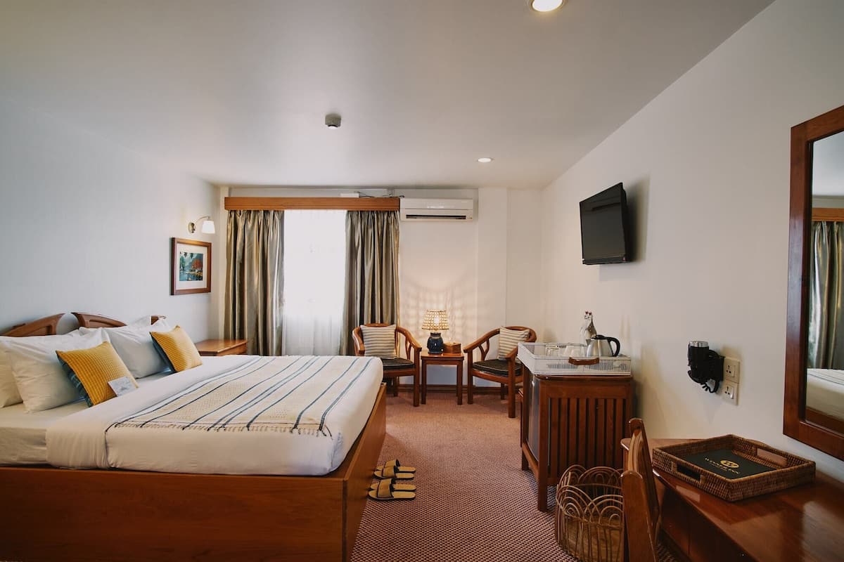 A hotel room with a bed, a desk, a chair, a television, and a window with curtains.