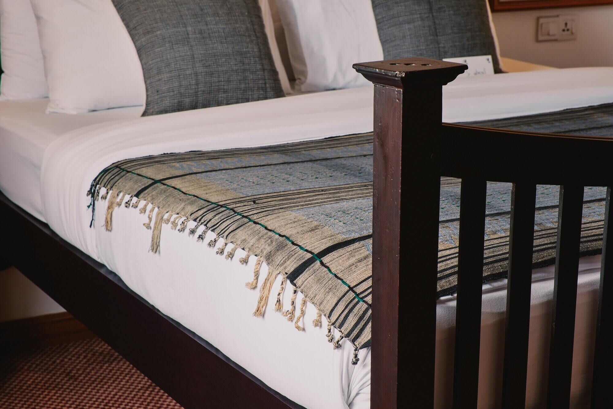 A bed with a white mattress, a dark wooden headboard, and a woven blanket with fringes.
