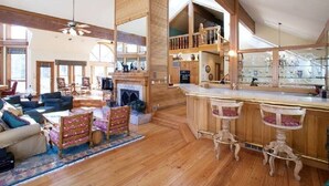 Un salón amplio con chimenea, piso de madera y techo alto con vigas a la vista.