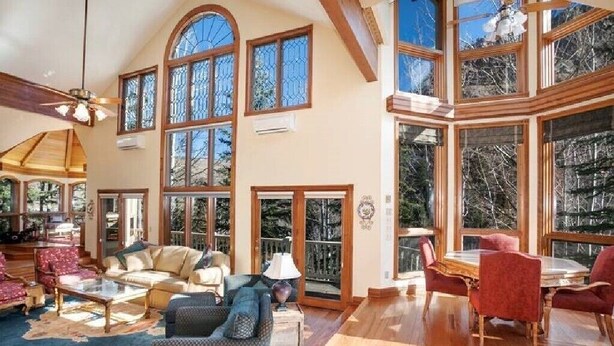 Un salón amplio con techo alto, ventanas grandes y una zona de comedor con sillas rojas.