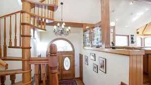 Una escalera de madera que conduce a un segundo piso, un candelabro, un amplio arco de entrada y una barra con cuadros enmarcados.
