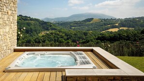 Ein Whirlpool auf einer Holzterrasse mit einer Steinmauer, mit Blick auf ein üppiges Tal mit Hügeln und einer fernen Bergkette.