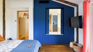 Ein Schlafzimmer mit blauer Akzentwand, Holzbalken, einem Fernseher und einem Fenster.