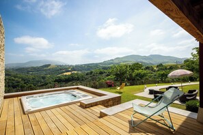 A wooden deck with a hot tub, outdoor seating, and a view of rolling hills.