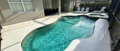 A swimming pool with a curved design, surrounded by a covered patio area with lounge chairs.