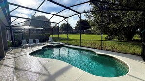 A swimming pool with a curved edge, surrounded by a covered area with chairs and a fence.