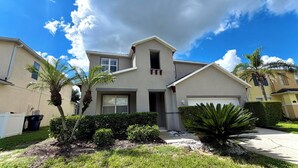 A residential house with a garage, a front yard with palm trees and shrubs, and a clear sky.