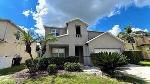 A residential house with a garage, a front yard with palm trees and shrubs, and a clear sky.