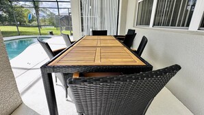 Eine überdachte Terrasse mit Pool, einem Holztisch und Korbstühlen.