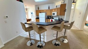 A modern kitchen with a central island, bar stools, and wooden cabinets. - Charming Pool Home, with game room. 15 minutes from Disney parks. (Davenport)