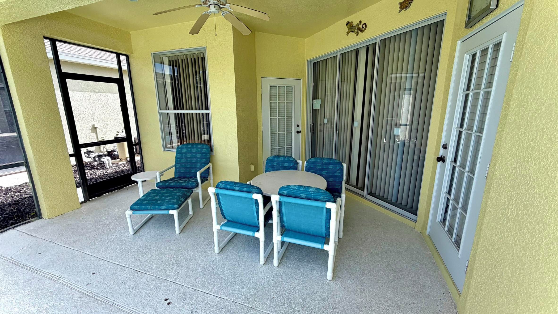 A covered patio area with a ceiling fan, a round table, and blue chairs.