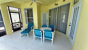 A covered patio area with a ceiling fan, a round table, and blue chairs. - Charming Pool Home, with game room. 15 minutes from Disney parks. (Davenport)