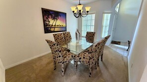 A dining area with a glass table and patterned chairs, a painting on the wall, and a chandelier. - Charming Pool Home, with game room. 15 minutes from Disney parks. (Davenport)