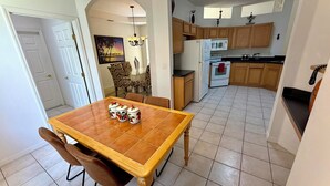 A dining area with a wooden table and chairs, a kitchen with wooden cabinets and appliances, and a hallway with a door and a painting. - Charming Pool Home, with game room. 15 minutes from Disney parks. (Davenport)